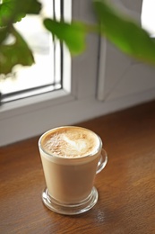 Photo of Cup of aromatic coffee with foam on wooden windowsill