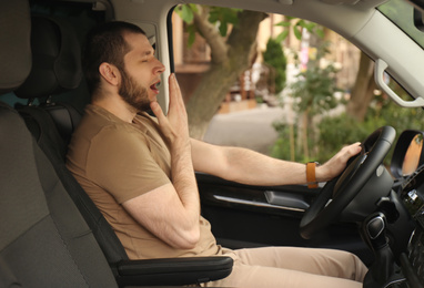 Tired man yawning while driving his modern car