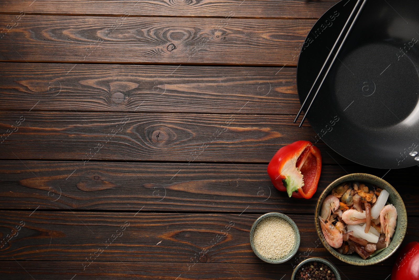 Photo of Black wok, chopsticks and products on wooden table, flat lay. Space for text