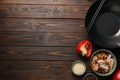 Photo of Black wok, chopsticks and products on wooden table, flat lay. Space for text