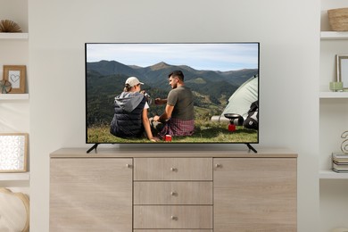Modern TV set on wooden stand in room. Scene of adventure movie on screen
