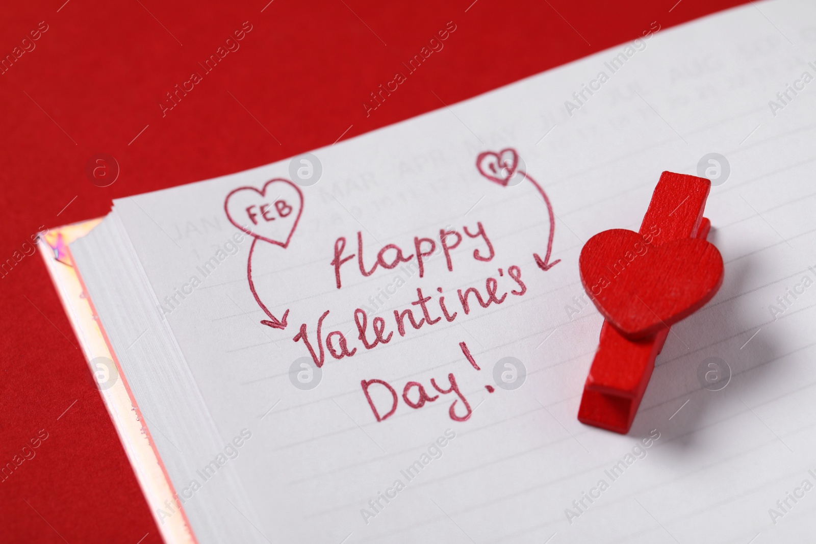 Photo of Notebook with text Happy Valentine's Day! and clothespin on red background, closeup
