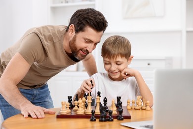 Father teaching his son to play chess following online lesson at home