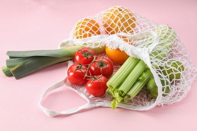 Photo of String bag with different vegetables and fruits on pink background