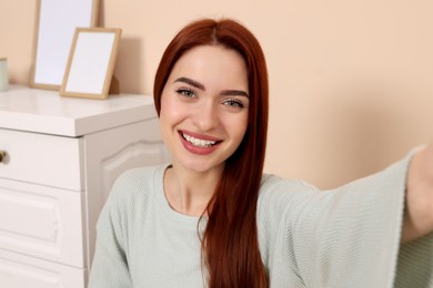 Photo of Happy woman with red dyed hair taking selfie at home