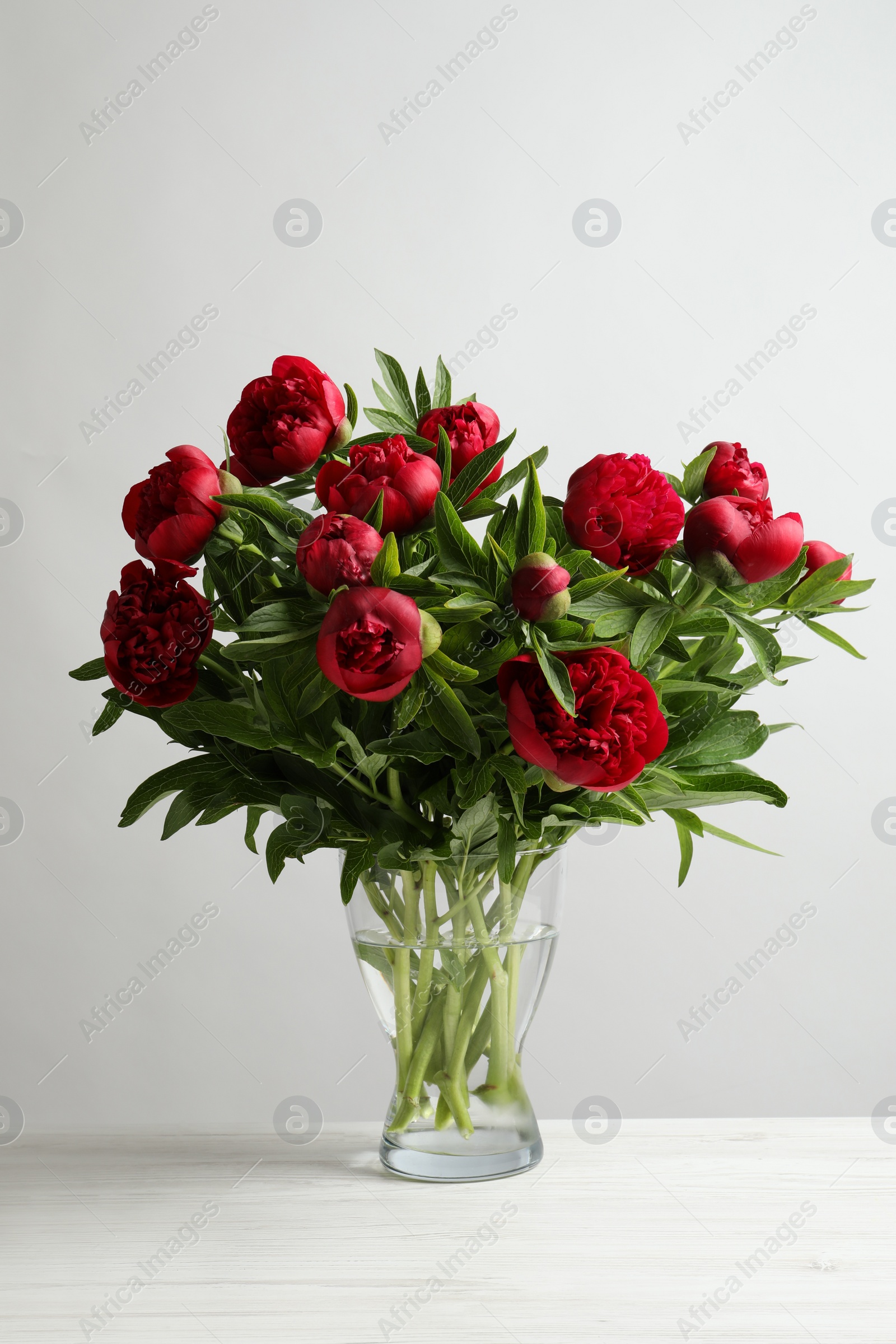 Photo of Beautiful bouquet of red peony flowers in glass vase on white table