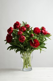 Photo of Beautiful bouquet of red peony flowers in glass vase on white table