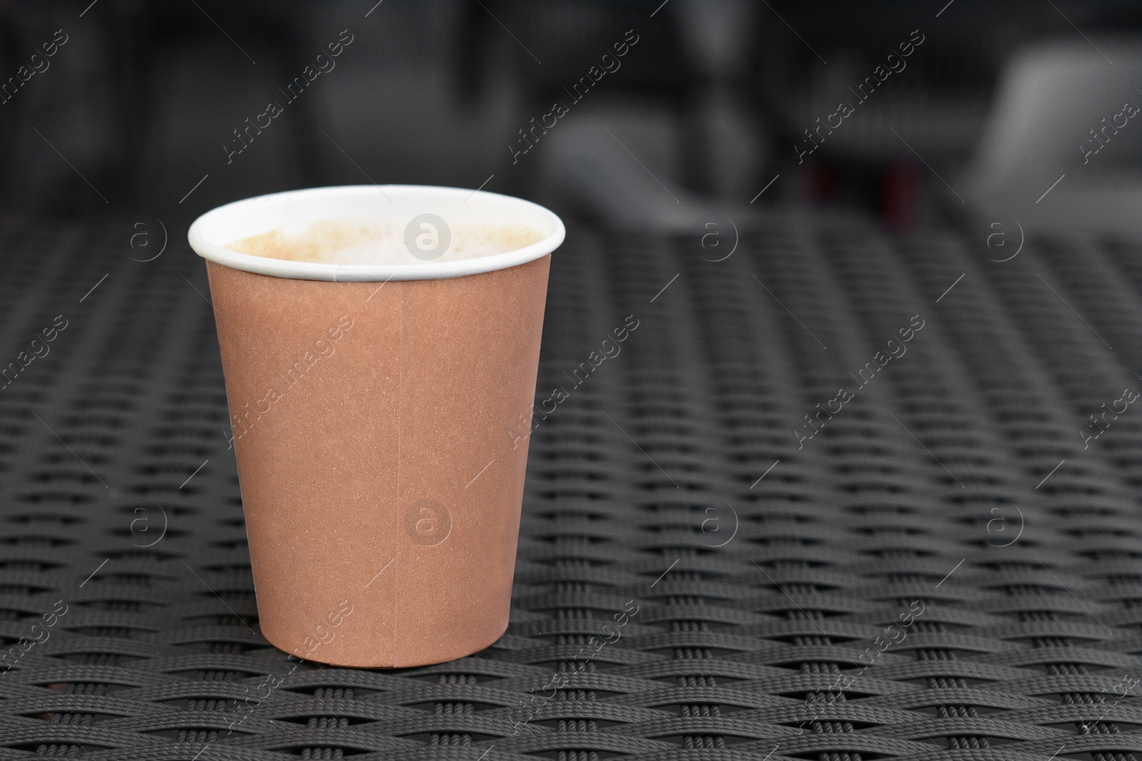 Photo of Cardboard cup with coffee on rattan table, closeup. Space for text