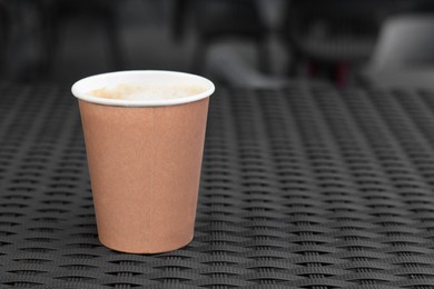 Photo of Cardboard cup with coffee on rattan table, closeup. Space for text