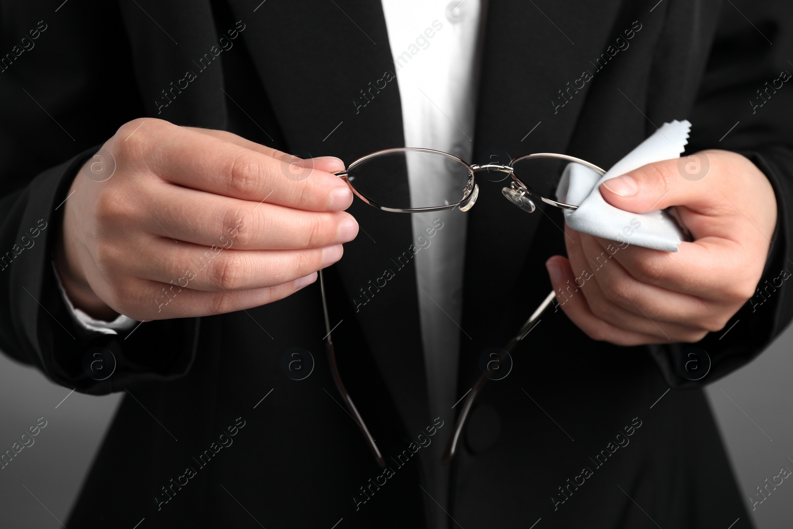 Photo of Woman wiping glasses with microfiber cloth on light grey background, closeup