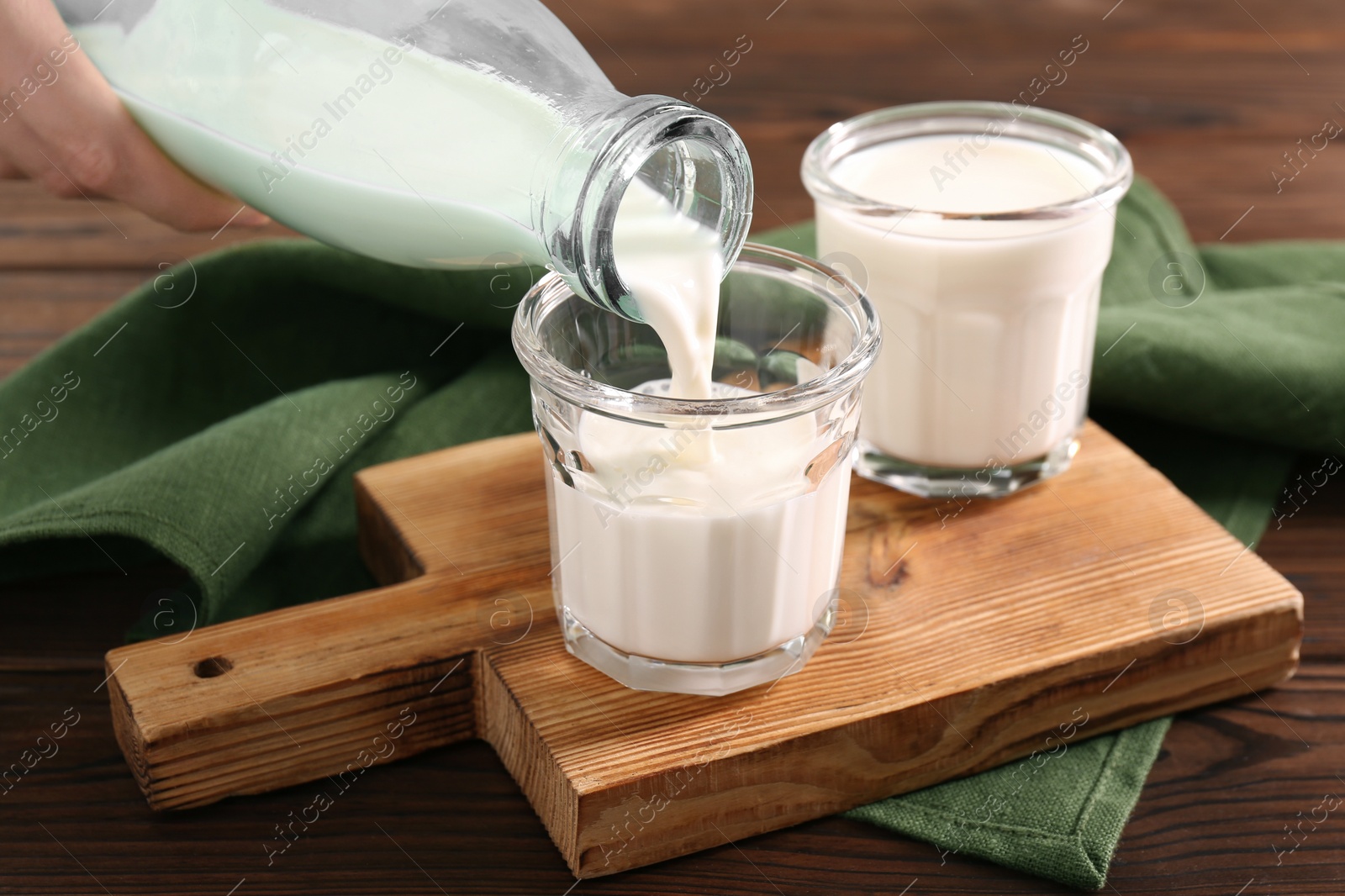 Photo of Pouring milk from bottle into glass at wooden table, closeup