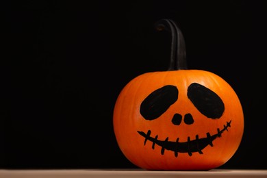 Photo of Halloween celebration. Pumpkin with drawn face on wooden table against black background, space for text
