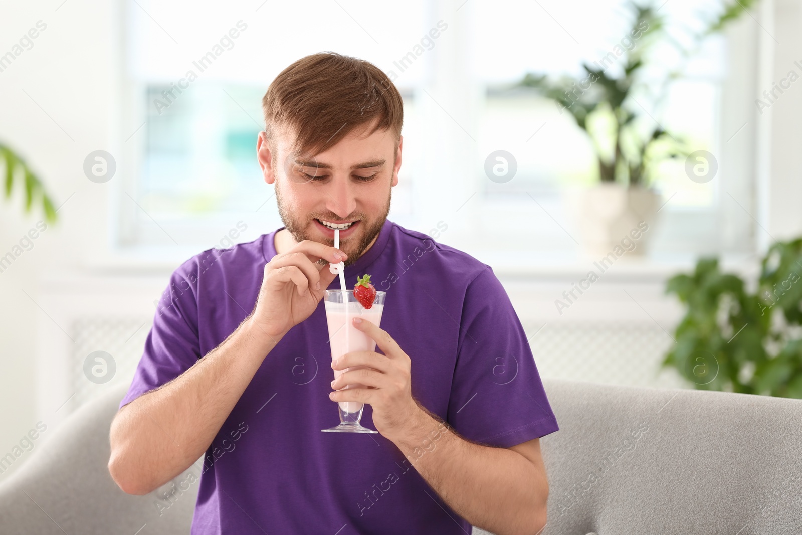 Photo of Young man with glass of delicious milk shake indoors