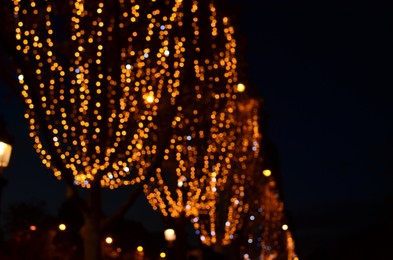 Photo of Blurred view of street with beautiful lights on trees at night. Bokeh effect