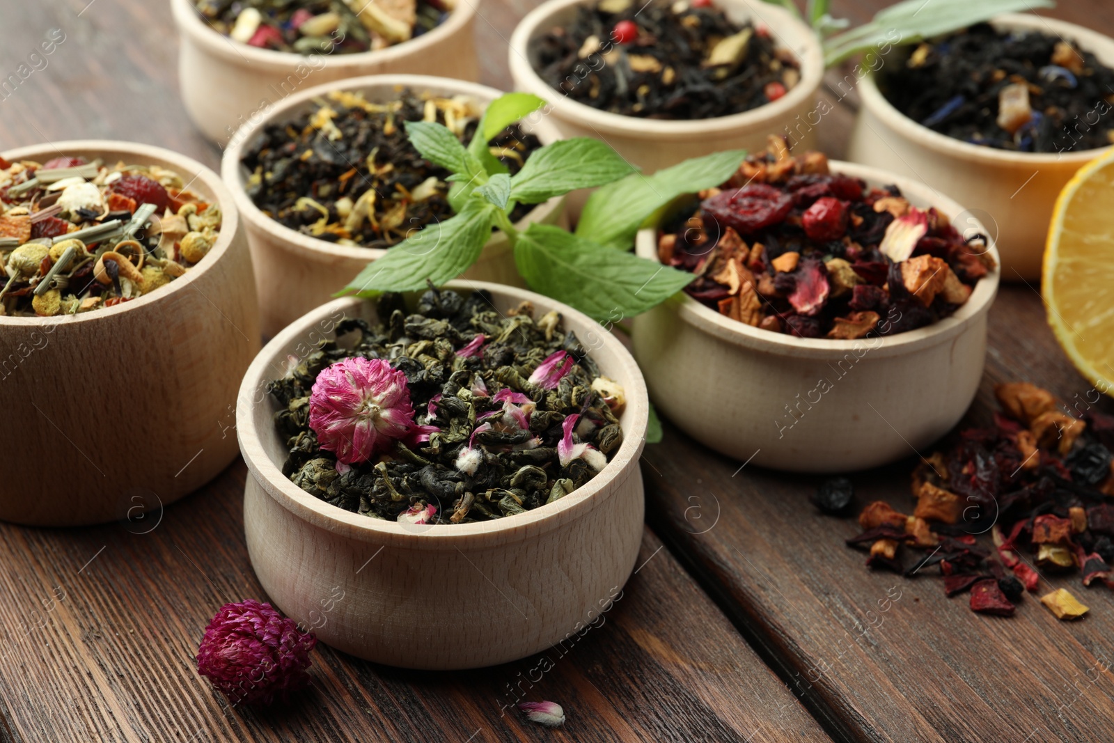 Photo of Different kinds of dry herbal tea in bowls on wooden table