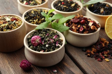 Different kinds of dry herbal tea in bowls on wooden table