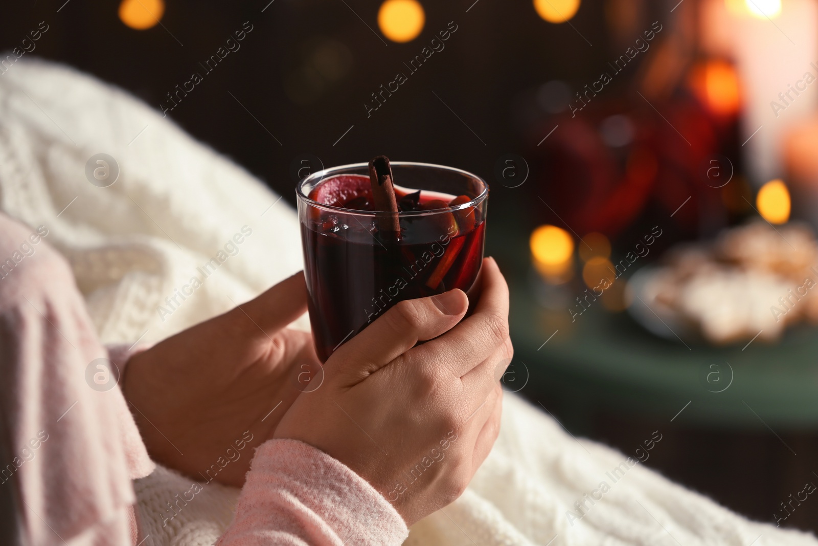 Photo of Woman with glass of mulled wine at home, focus on hands. Space for text