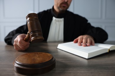 Photo of Judge with gavel and book sitting at wooden table indoors, closeup