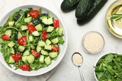 Photo of Delicious salad with cucumbers, tomatoes and sesame in bowl served on light table, flat lay