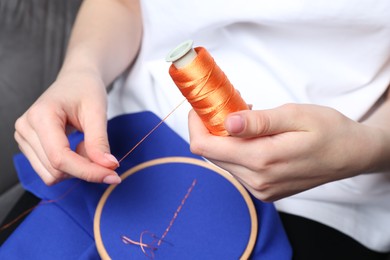 Woman with spool of thread embroidering on cloth, closeup