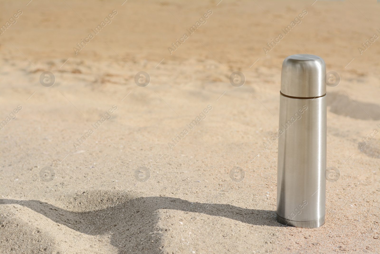 Photo of Metallic thermos with hot drink on sandy beach, space for text