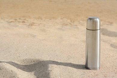 Photo of Metallic thermos with hot drink on sandy beach, space for text