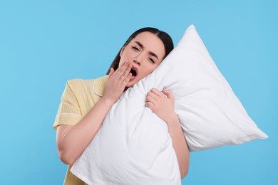 Photo of Tired young woman with pillow yawning on light blue background. Insomnia problem