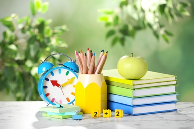 Photo of Alarm clock, apple and school stationery on white marble table