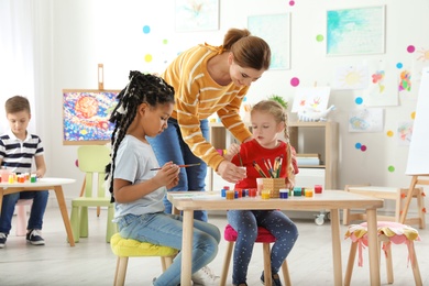 Children with female teacher at painting lesson indoors