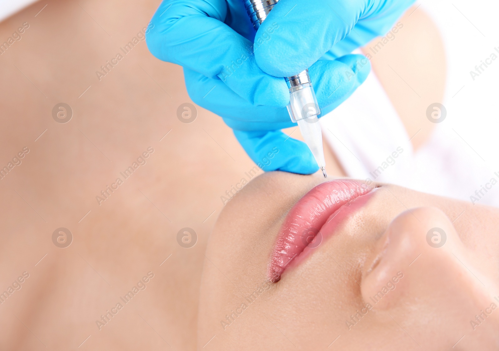 Photo of Young woman getting permanent makeup on lips in beautician salon, closeup