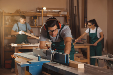 Photo of Professional carpenter working with surface planer and colleagues in workshop