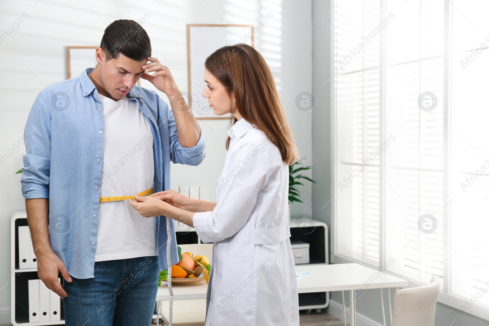 Photo of Young nutritionist measuring patient's waist in clinic