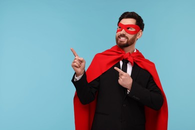Photo of Businessman wearing red superhero cape and mask on light blue background