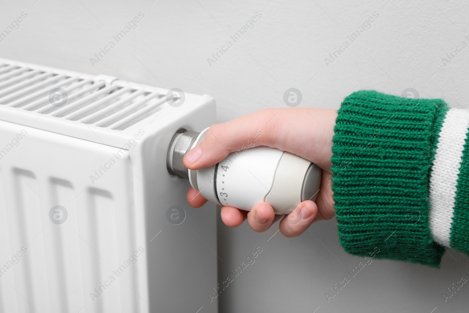 Photo of Girl adjusting heating radiator thermostat near white wall indoors, closeup