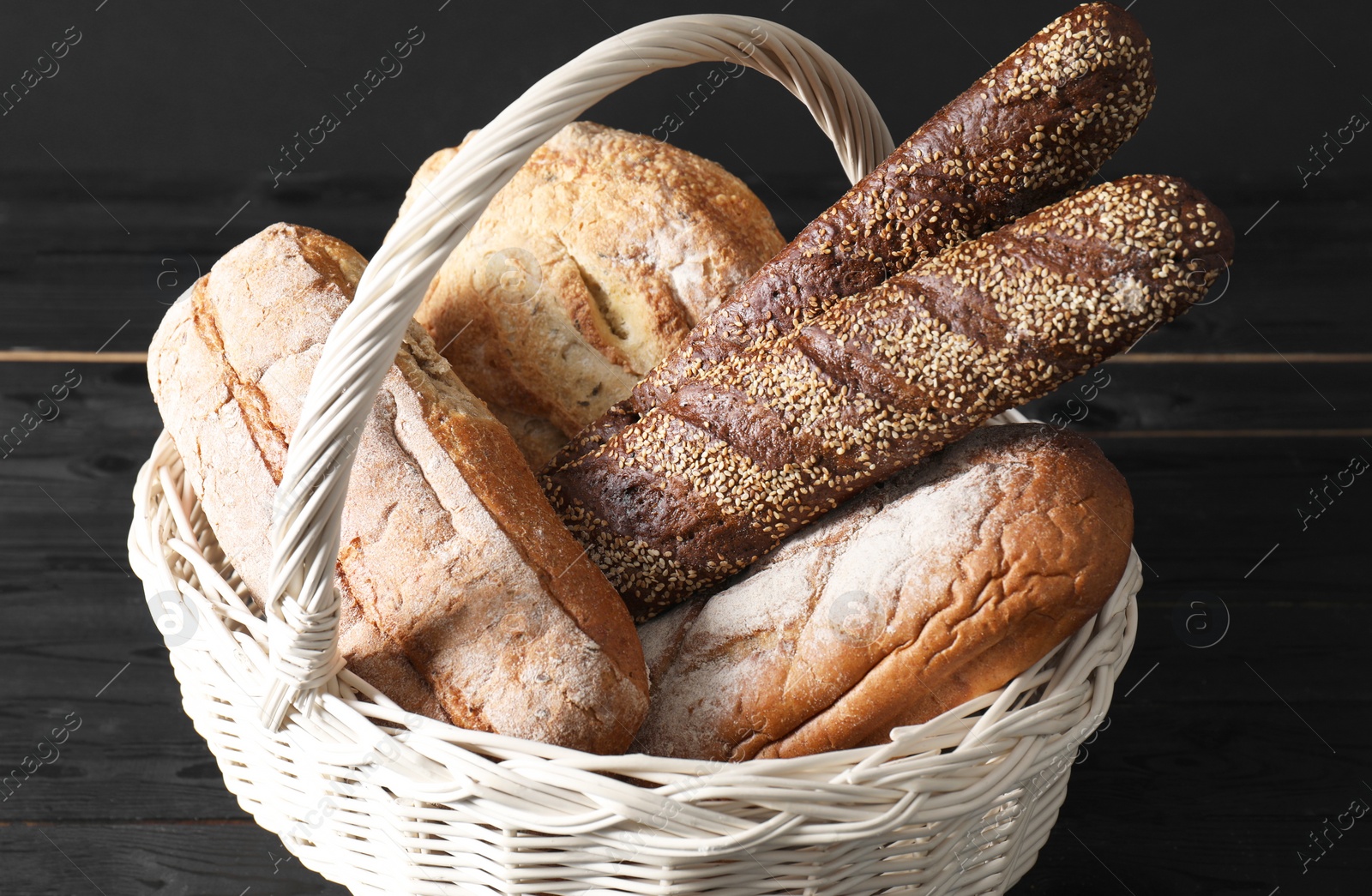 Photo of Wicker basket with different types of fresh bread on black wooden table