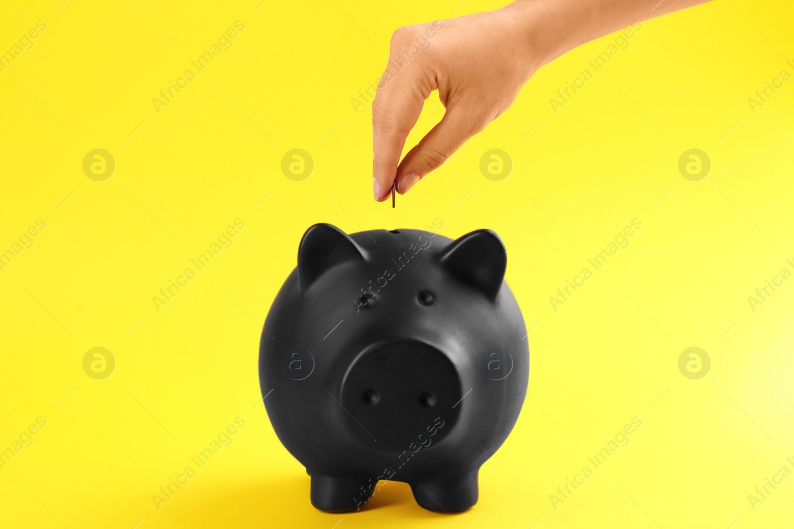 Photo of Woman putting coin into piggy bank on yellow background, closeup