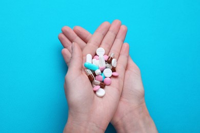 Woman holding colorful antidepressants on light blue background, top view