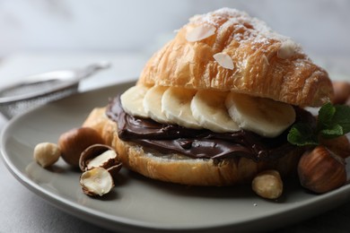 Delicious croissant with banana, chocolate and hazelnuts on grey table, closeup