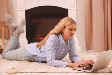 Young woman working on laptop near fireplace in room