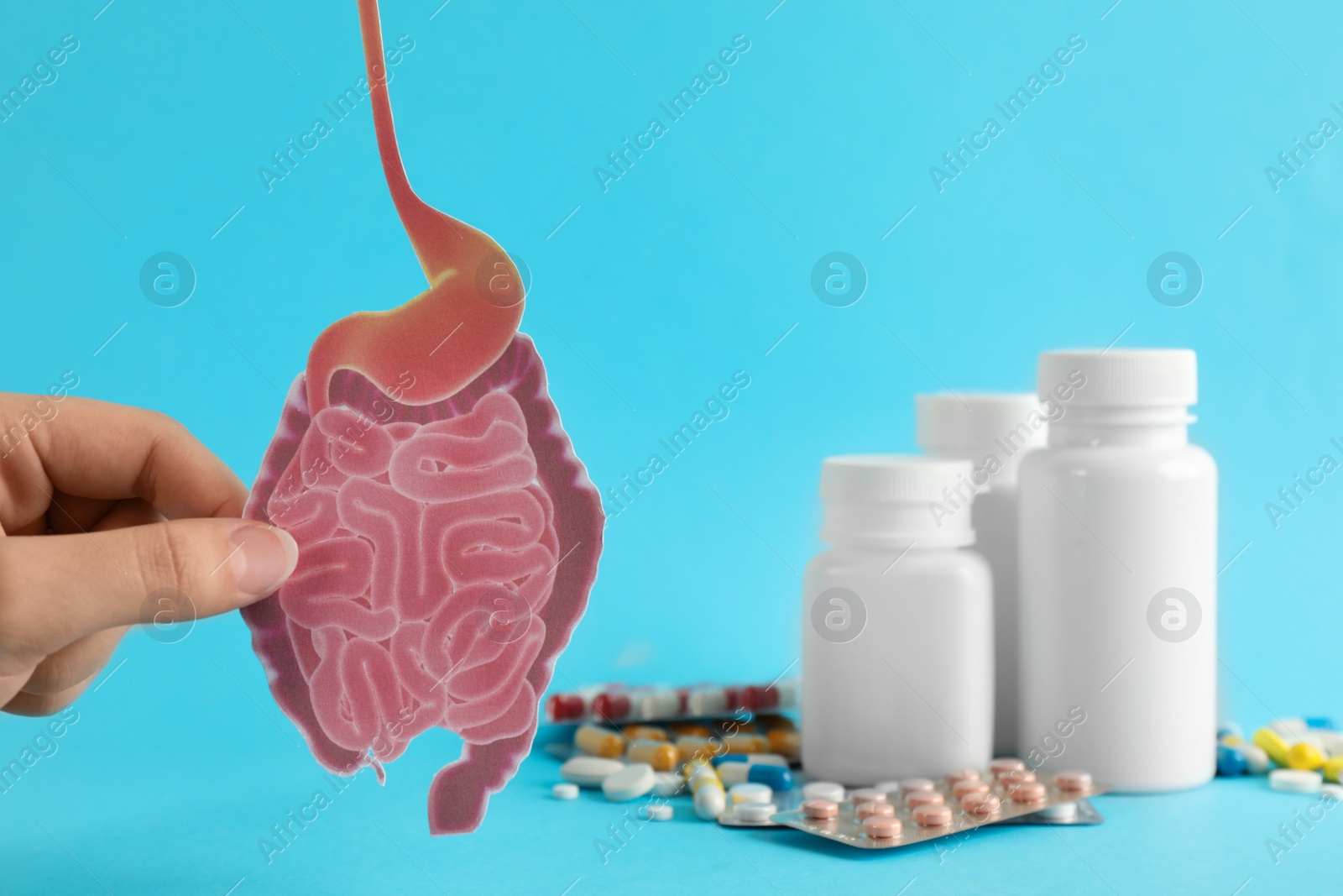 Photo of Woman holding paper intestine cutout near pills on turquoise background, closeup
