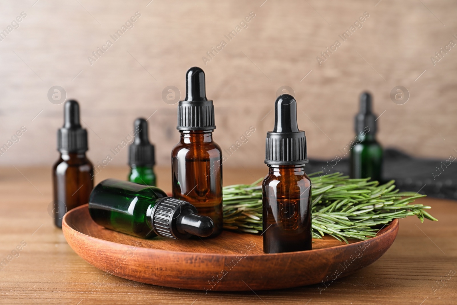 Photo of Plate with bottles of essential oils and rosemary on wooden table