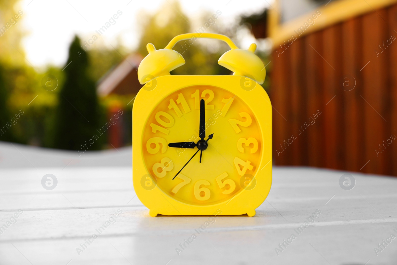 Photo of Yellow alarm clock on white wooden table outdoors at sunny morning