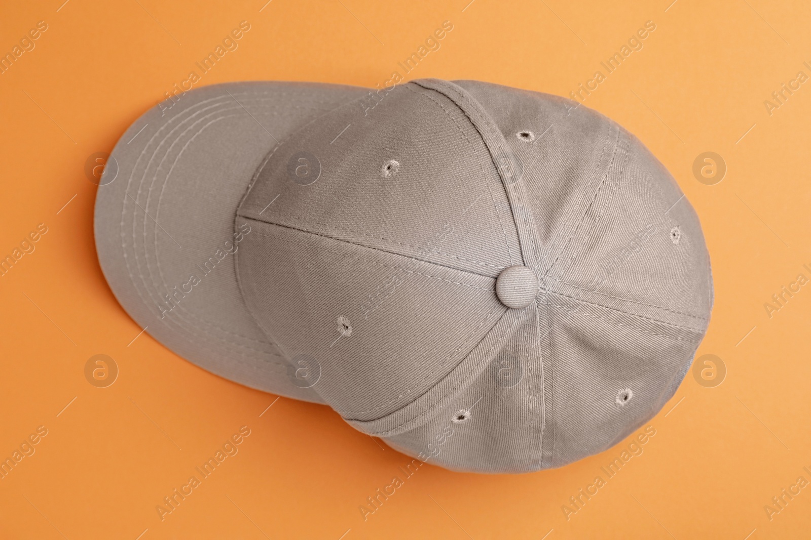 Photo of Stylish grey baseball cap on orange background, top view