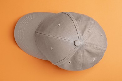 Stylish grey baseball cap on orange background, top view