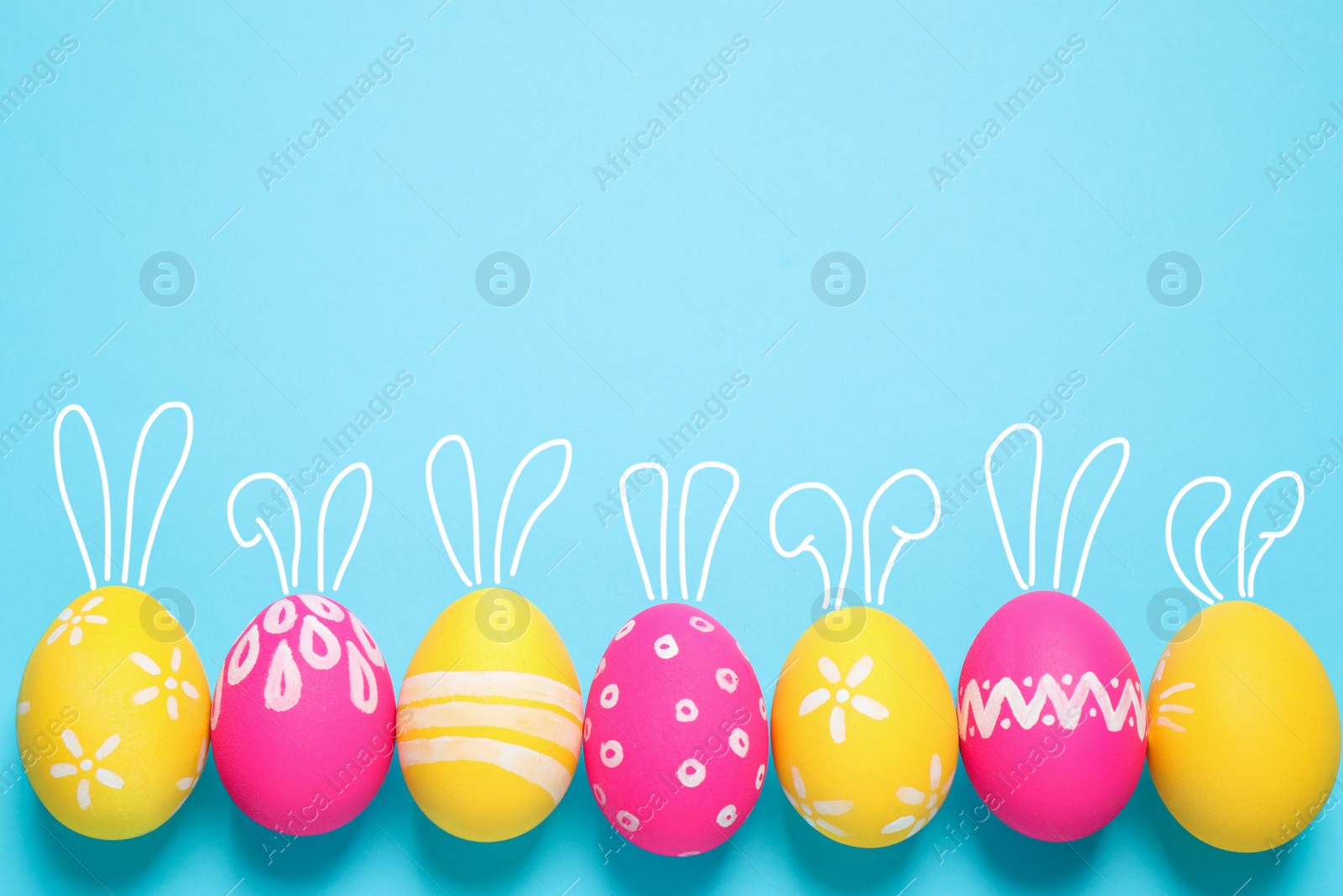 Image of Bright Easter eggs with cute bunny ears and space for text on light blue background, flat lay