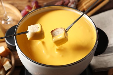 Photo of Dipping pieces of bread into tasty cheese fondue, closeup