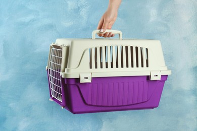 Photo of Woman holding violet pet carrier against light blue wall, closeup