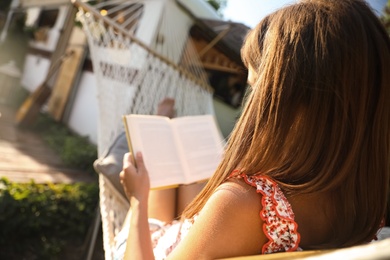 Photo of Young woman reading book in hammock near motorhome outdoors on sunny day