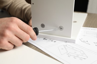 Photo of Man with screwdriver assembling white furniture at table, closeup