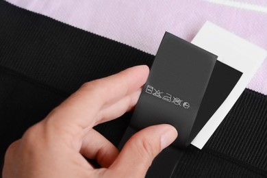 Photo of Woman holding clothing label on black garment, closeup